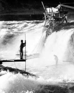 Fishing in the mists at Celilo Falls. The platforms were built on small basalt islands in the middle of the river channel. These highly productive sites were reachable only by a system of hand-operated cable cars. Photo copyright © 1950 Wilma Roberts.